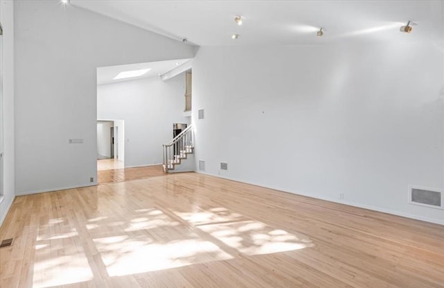 unfurnished living room featuring light hardwood / wood-style flooring, high vaulted ceiling, and a skylight