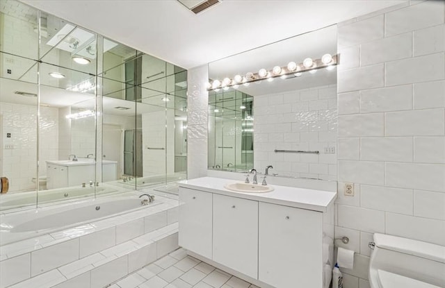 bathroom featuring toilet, tile walls, vanity, a relaxing tiled tub, and tile patterned flooring