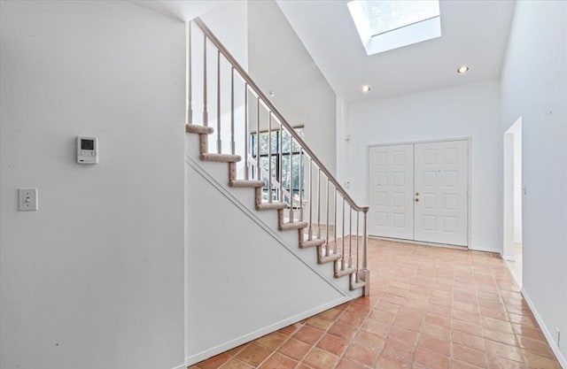 entrance foyer featuring light tile patterned floors, high vaulted ceiling, and a skylight