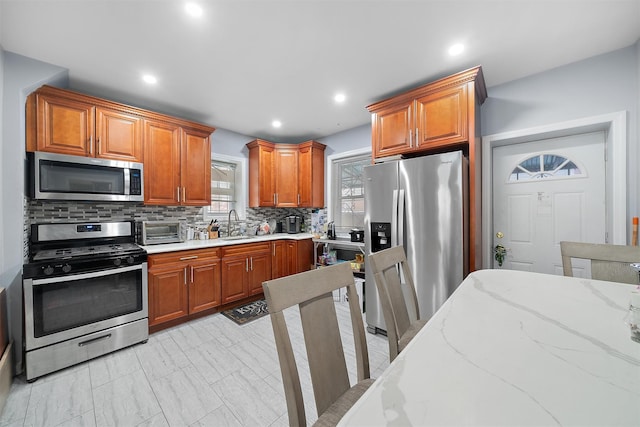 kitchen featuring decorative backsplash, appliances with stainless steel finishes, brown cabinets, light stone countertops, and recessed lighting