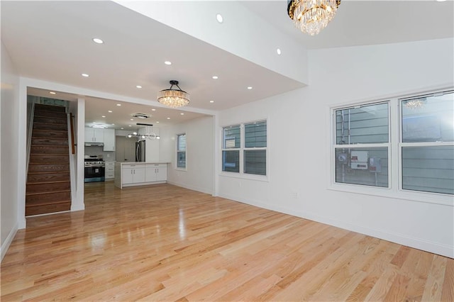 unfurnished living room with light wood-type flooring and a notable chandelier