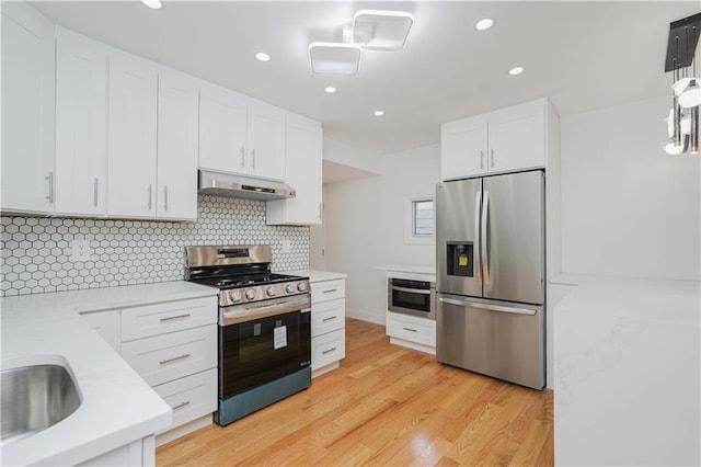 kitchen featuring hanging light fixtures, white cabinets, stainless steel appliances, light hardwood / wood-style floors, and backsplash