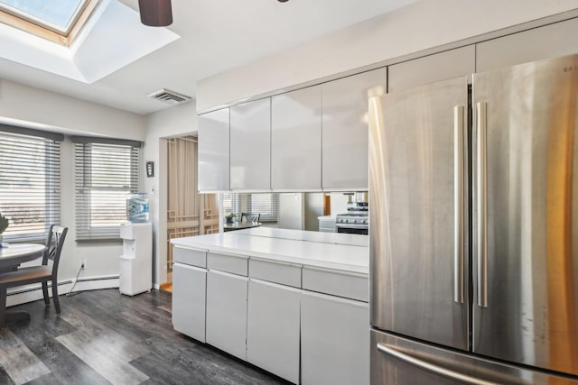 kitchen with dark wood-type flooring, a skylight, stainless steel refrigerator, a baseboard radiator, and white cabinets