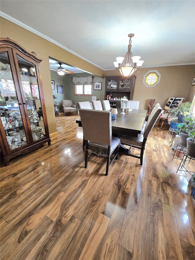 dining area with ceiling fan with notable chandelier, wood-type flooring, and ornamental molding