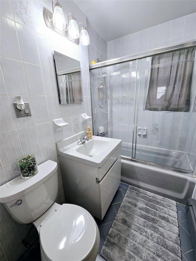 full bathroom featuring tile patterned floors, toilet, combined bath / shower with glass door, tile walls, and vanity