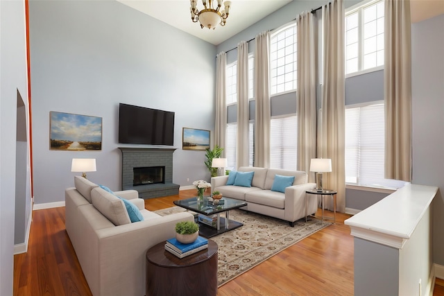 living room featuring hardwood / wood-style flooring, a brick fireplace, a towering ceiling, and an inviting chandelier