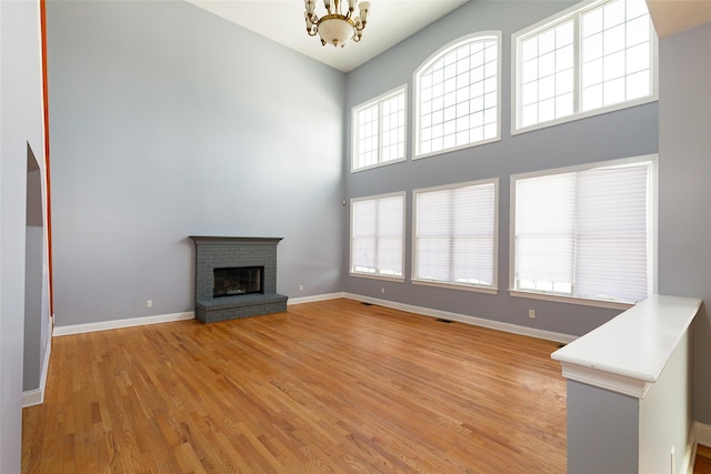 unfurnished living room featuring a brick fireplace, a towering ceiling, a chandelier, and light hardwood / wood-style flooring