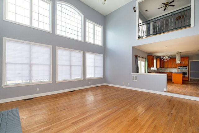 unfurnished living room featuring a notable chandelier, light hardwood / wood-style floors, and a high ceiling