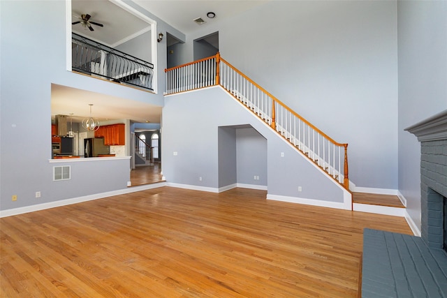 unfurnished living room featuring ceiling fan with notable chandelier, light hardwood / wood-style floors, a brick fireplace, and a high ceiling