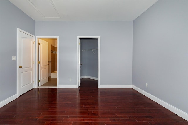 unfurnished bedroom featuring ensuite bathroom, a spacious closet, dark hardwood / wood-style flooring, and a closet