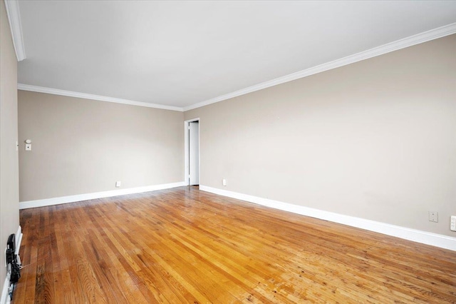 empty room featuring crown molding, wood finished floors, and baseboards