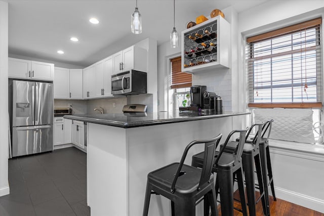 kitchen with a breakfast bar, white cabinetry, hanging light fixtures, kitchen peninsula, and stainless steel appliances