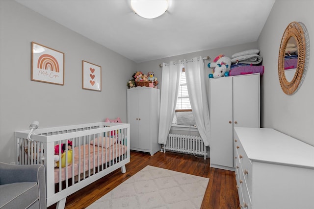 bedroom featuring dark hardwood / wood-style flooring, radiator, and a crib