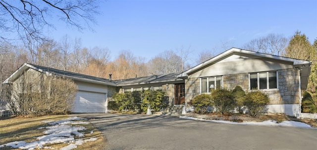 ranch-style house with an attached garage, stone siding, and aphalt driveway