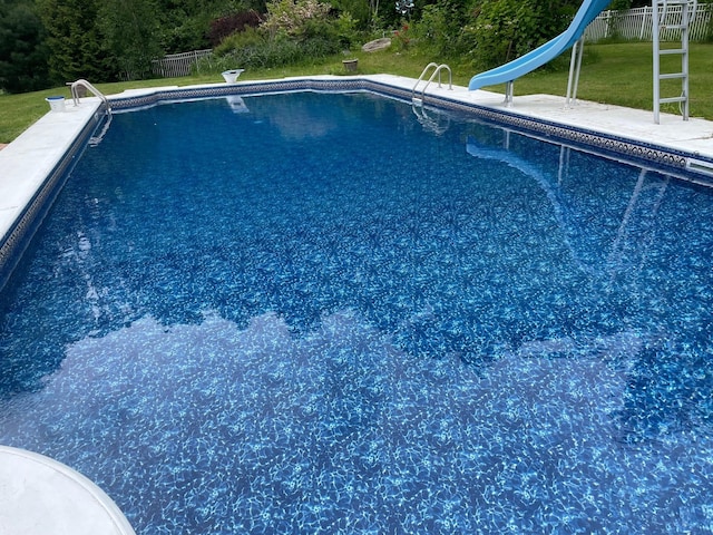 pool featuring a water slide, a patio area, fence, and a lawn