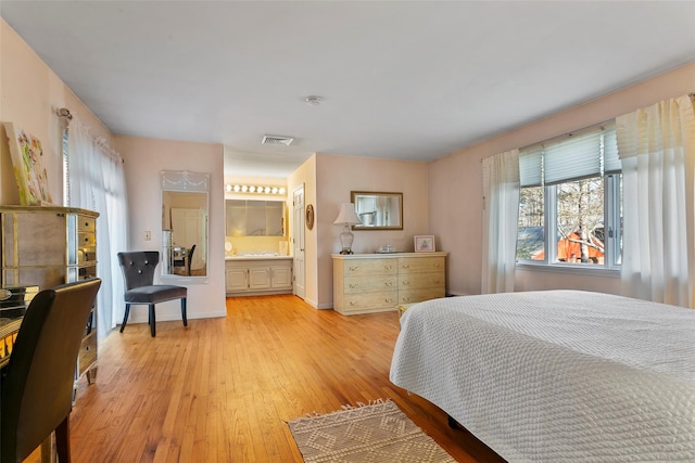 bedroom featuring light wood-style floors, ensuite bath, and visible vents