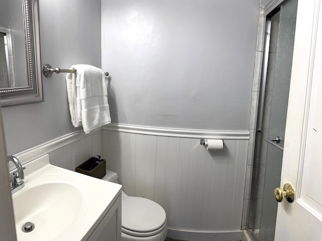 full bath with wainscoting, a shower with door, vanity, and toilet