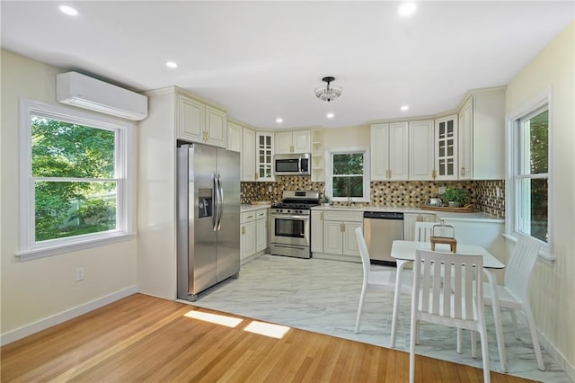 kitchen featuring stainless steel appliances, backsplash, an AC wall unit, and a healthy amount of sunlight