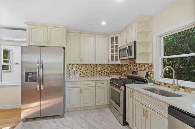 kitchen featuring light stone counters, a sink, decorative backsplash, cream cabinetry, and appliances with stainless steel finishes