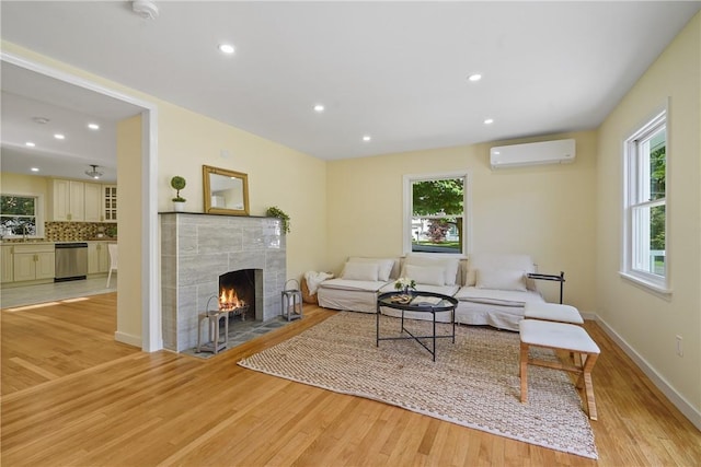 living area featuring a wall mounted air conditioner, light wood-style flooring, and a tiled fireplace