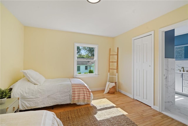 bedroom with baseboards, light wood-style flooring, a closet, ensuite bath, and a sink