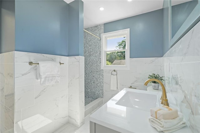 full bath with a wainscoted wall, tile walls, vanity, and a tile shower