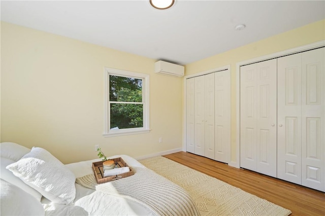 bedroom with a wall unit AC, wood finished floors, multiple closets, and baseboards