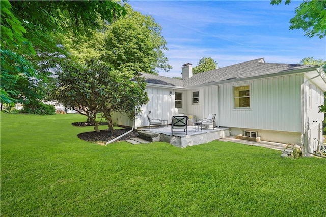 rear view of property with a patio area, a chimney, a yard, and a shingled roof