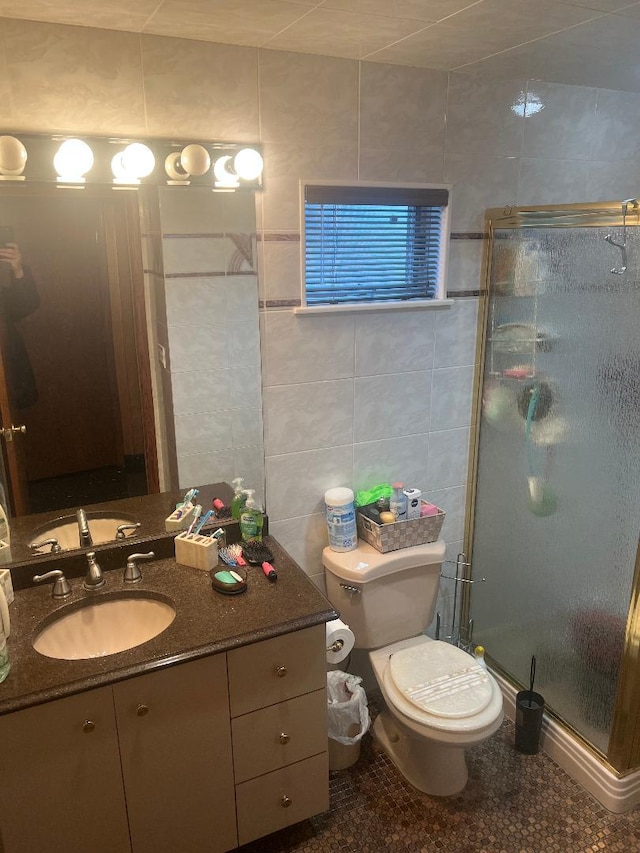 bathroom featuring a shower with door, vanity, tile walls, and toilet