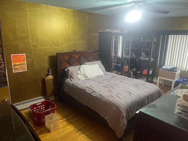 bedroom with a baseboard heating unit, hardwood / wood-style flooring, and ceiling fan