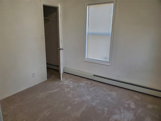 unfurnished bedroom featuring a walk in closet, light carpet, and a baseboard heating unit