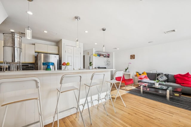 kitchen featuring a breakfast bar area, white cabinetry, stainless steel refrigerator, pendant lighting, and light hardwood / wood-style floors