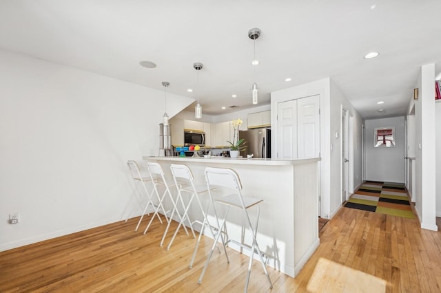 kitchen with a breakfast bar area, white cabinetry, hanging light fixtures, stainless steel appliances, and kitchen peninsula