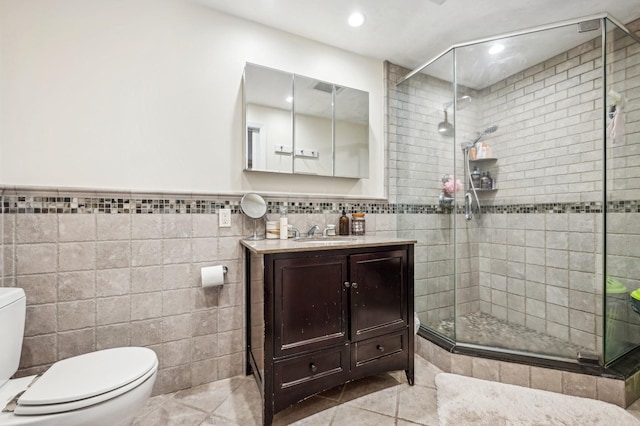 bathroom featuring tile patterned flooring, tile walls, vanity, a shower with shower door, and toilet