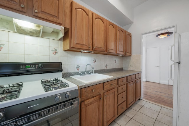 kitchen featuring sink, range with gas stovetop, light tile patterned flooring, decorative backsplash, and white fridge