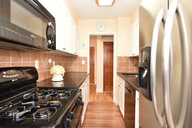 kitchen with tasteful backsplash, sink, white cabinets, black appliances, and light hardwood / wood-style flooring