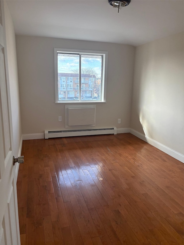 spare room with baseboard heating and dark hardwood / wood-style floors