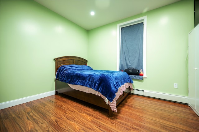 bedroom featuring a baseboard heating unit and hardwood / wood-style floors