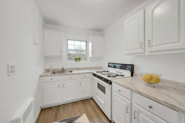 kitchen featuring white cabinetry, sink, light hardwood / wood-style flooring, and white gas range oven