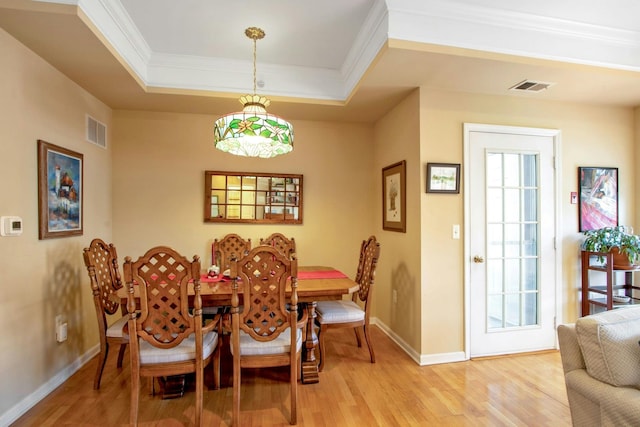 dining room featuring crown molding, a raised ceiling, and light hardwood / wood-style flooring