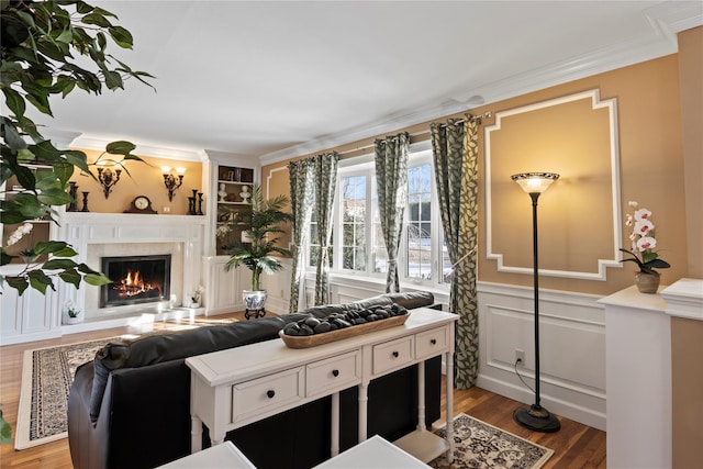 living room featuring built in shelves, a fireplace, hardwood / wood-style floors, and crown molding