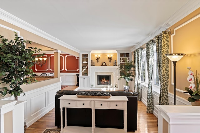 living room with hardwood / wood-style flooring, ornamental molding, built in features, and a chandelier