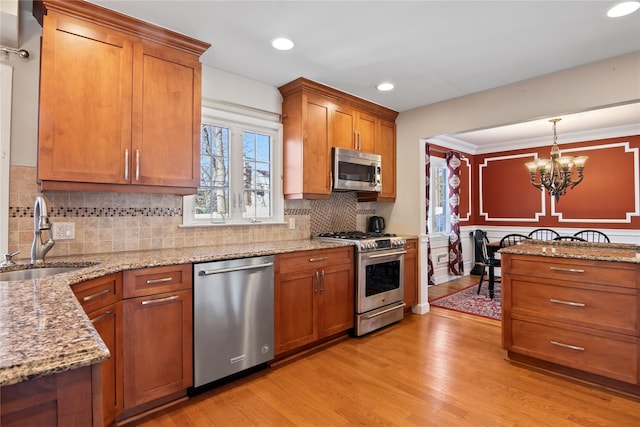 kitchen with sink, hanging light fixtures, stainless steel appliances, light stone countertops, and light wood-type flooring