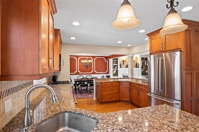 kitchen featuring pendant lighting, sink, stainless steel refrigerator, dark stone countertops, and kitchen peninsula