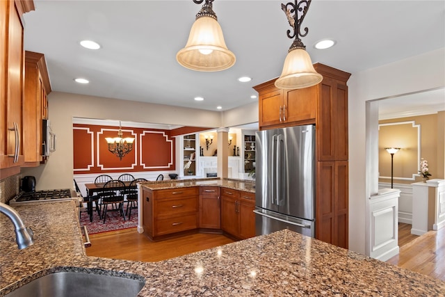 kitchen featuring appliances with stainless steel finishes, sink, hanging light fixtures, light hardwood / wood-style floors, and kitchen peninsula