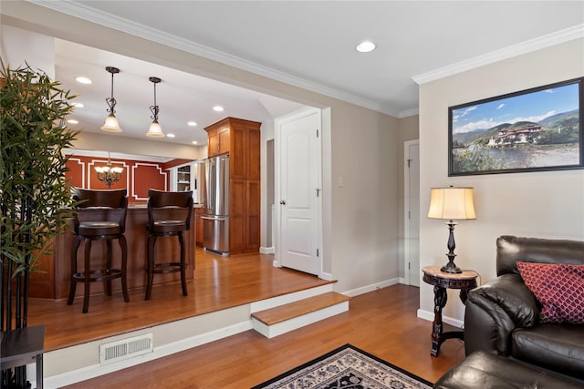 living room with a notable chandelier, ornamental molding, and light hardwood / wood-style floors