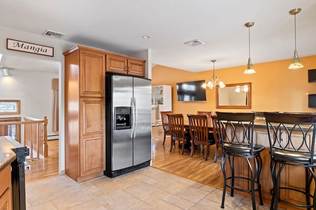 kitchen with a breakfast bar, dark stone counters, hanging light fixtures, baseboard heating, and stainless steel refrigerator with ice dispenser