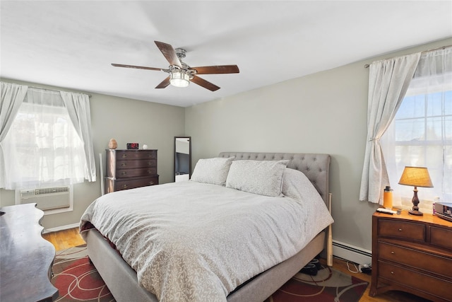 bedroom featuring ceiling fan, a baseboard radiator, multiple windows, and hardwood / wood-style flooring