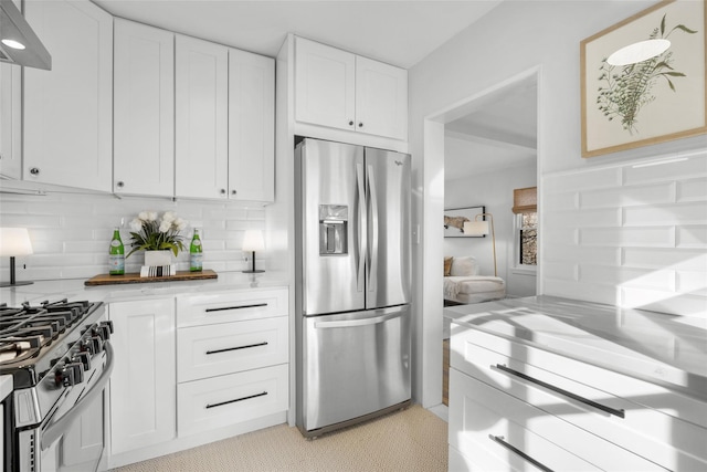 kitchen featuring white cabinetry, decorative backsplash, light stone counters, stainless steel appliances, and wall chimney range hood