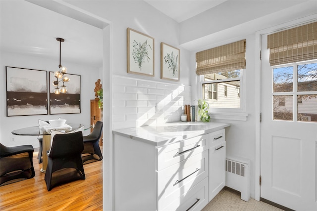 interior space featuring tasteful backsplash, a chandelier, radiator, pendant lighting, and white cabinets